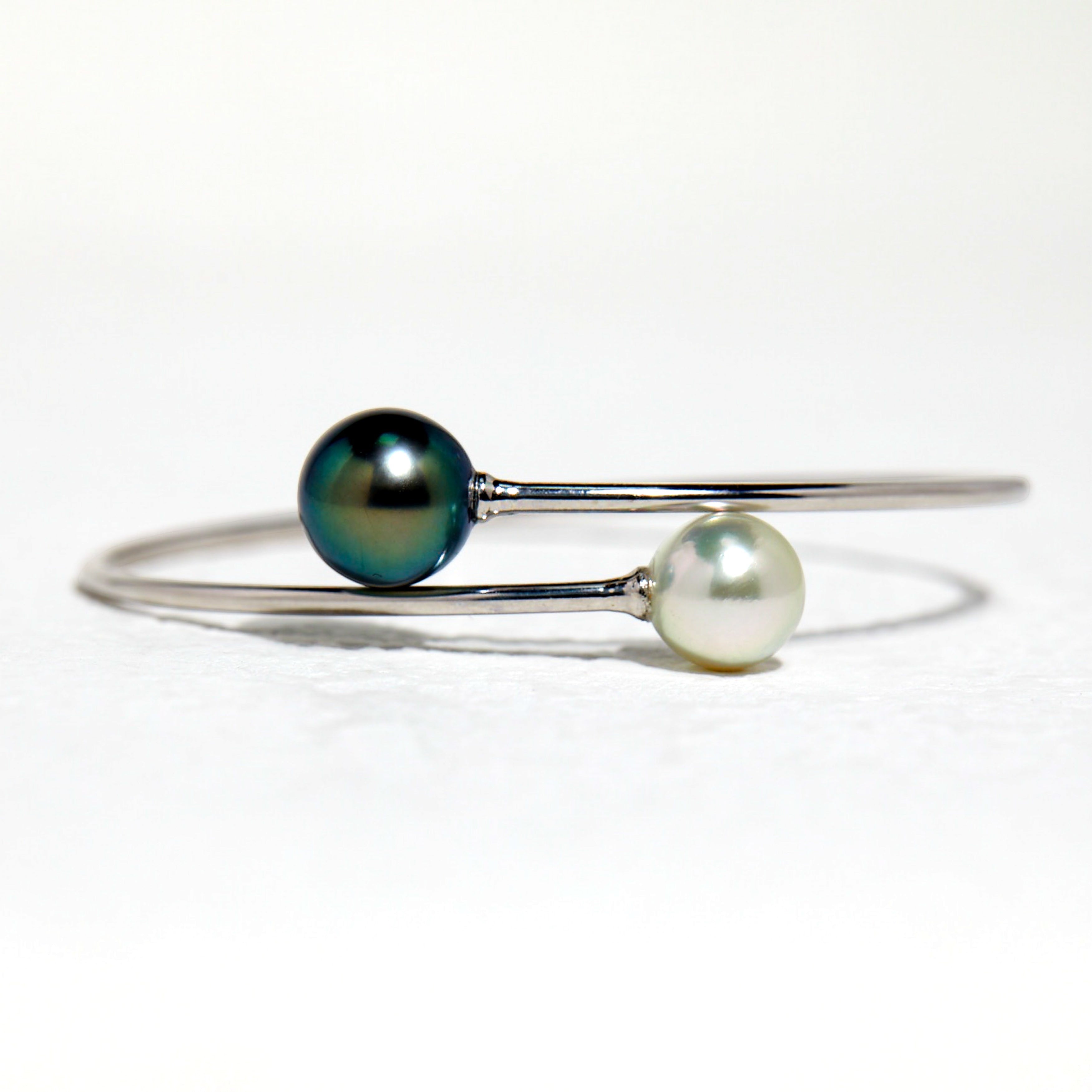 BoxUnboxed 18K white gold bypass bangle with a dark peacock Tahitian pearl and a white Akoya pearl.