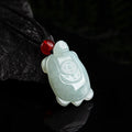 BoxUnboxed hand-carved natural jadeite turtle pendant with a red bead on a black cord against a dark background