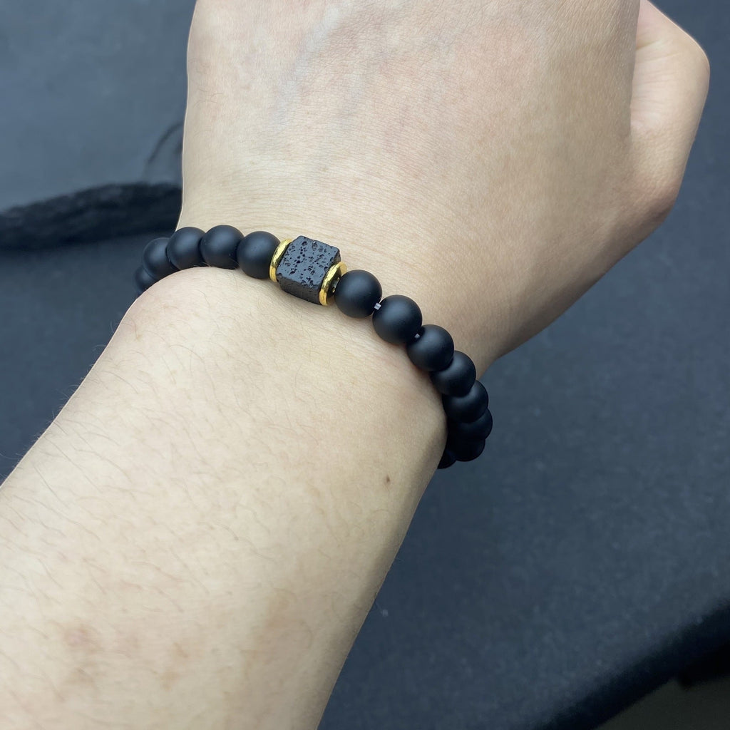 BoxUnboxed Obsidian & Volcanic Stone Stack Bracelet with matte black beads and a central textured cube bead with gold accents.